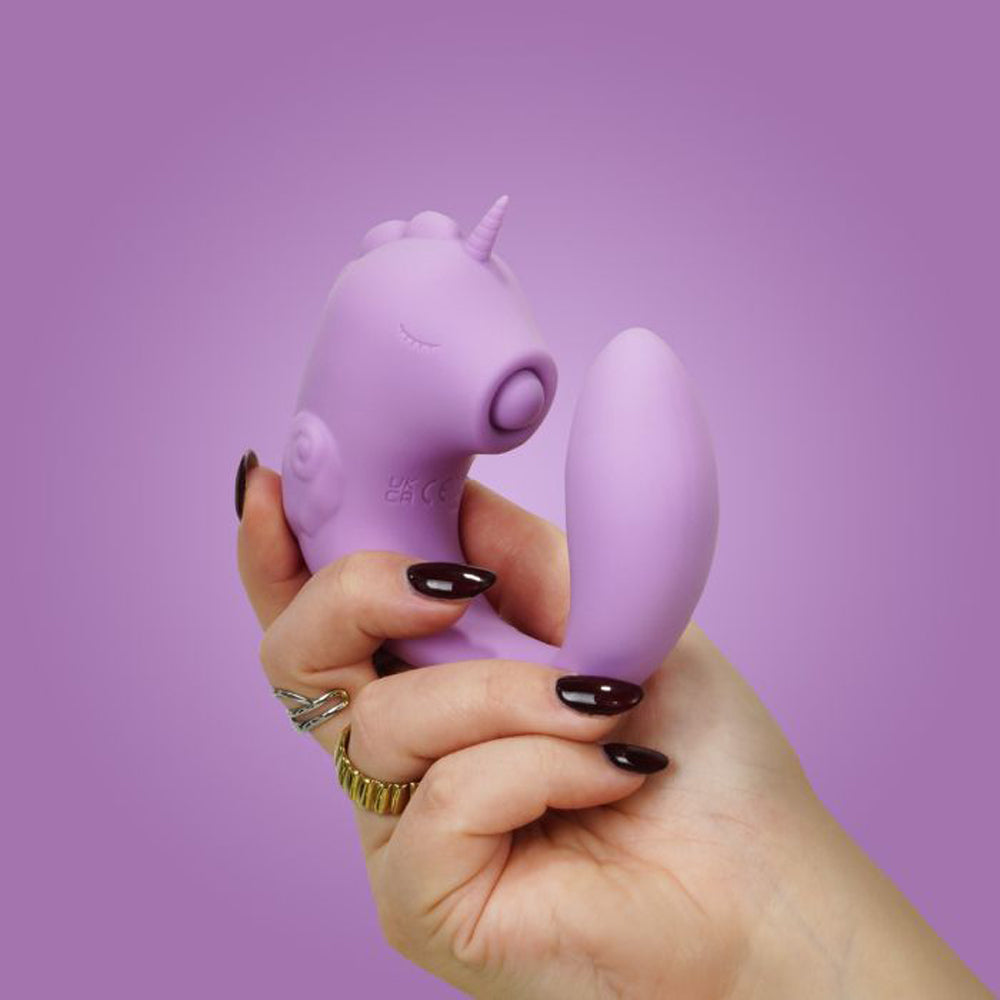 A purple unicorn-shaped massager held in a hand with dark nail polish.