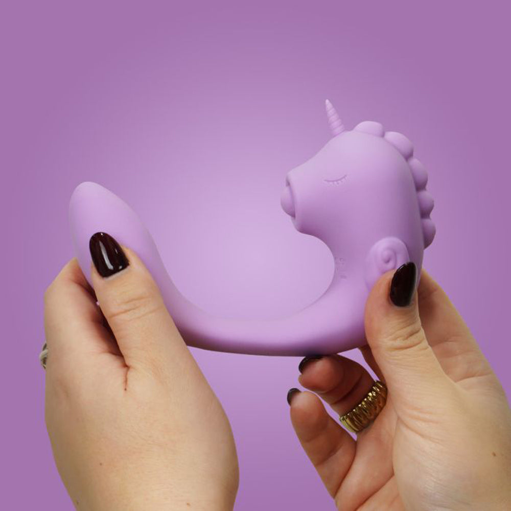 A purple unicorn-shaped silicone massager held by two hands.
