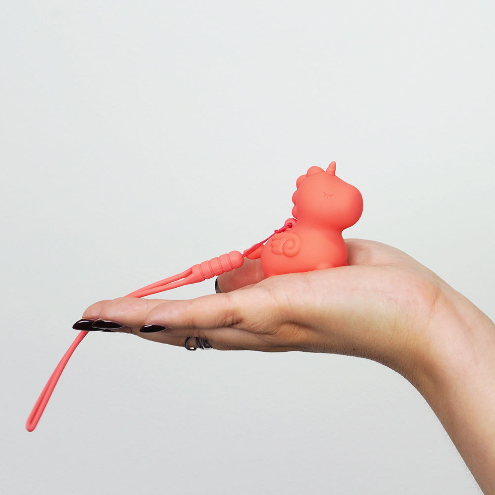 A pink unicorn-shaped silicone vibrator with a charging cord rests in a hand.