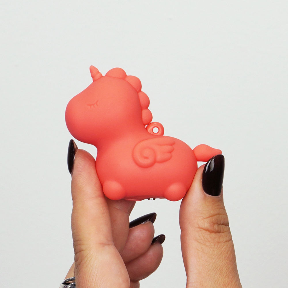 A coral pink silicone unicorn toy with wings is held between two fingers.