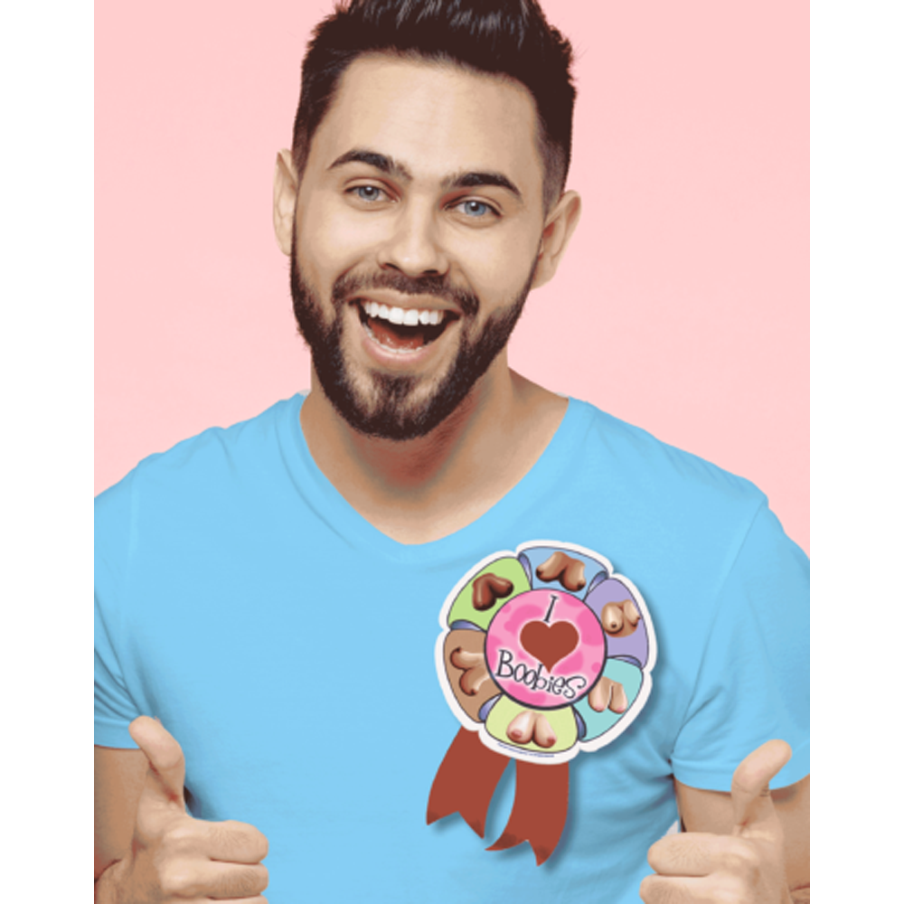 A man wears a large "I Love Boobies" ribbon pin on his blue t-shirt.