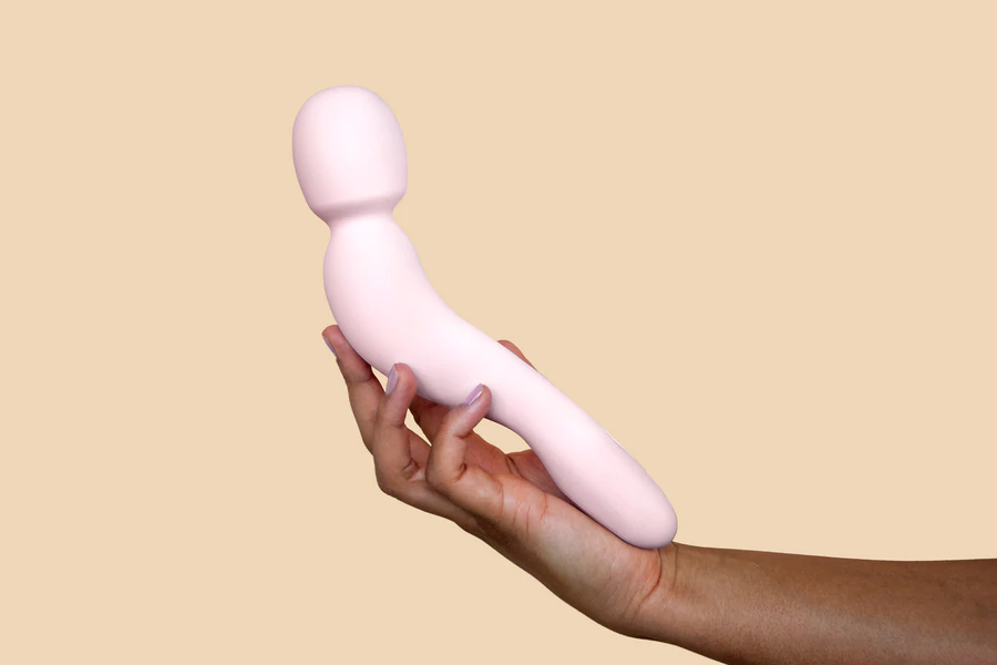 A pink curved wand vibrator held in a hand.