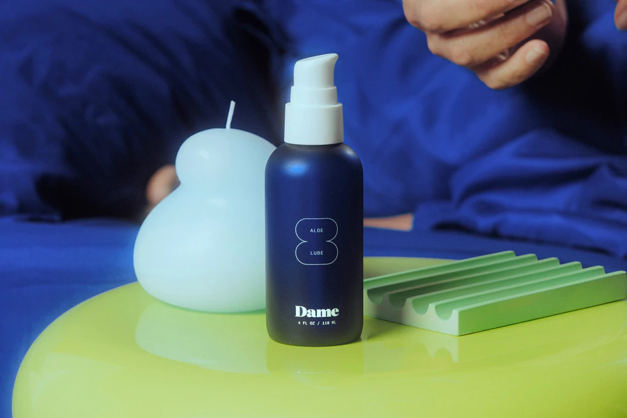 Dame Aloe Lube bottle with a white pump, next to a white candle and a green ribbed holder.