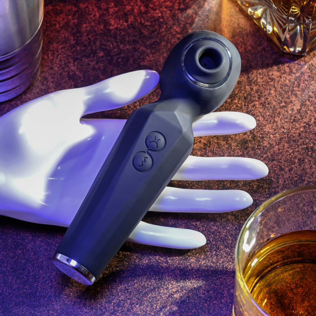 A grey dual motor wand vibrator with suction on a white hand prop.