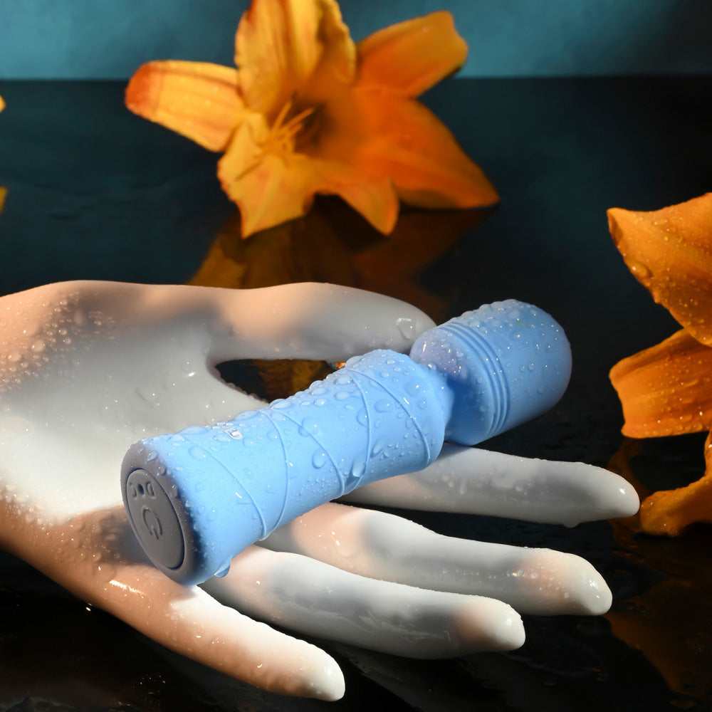 A blue waterproof mini wand vibrator with water droplets rests on a white surface.