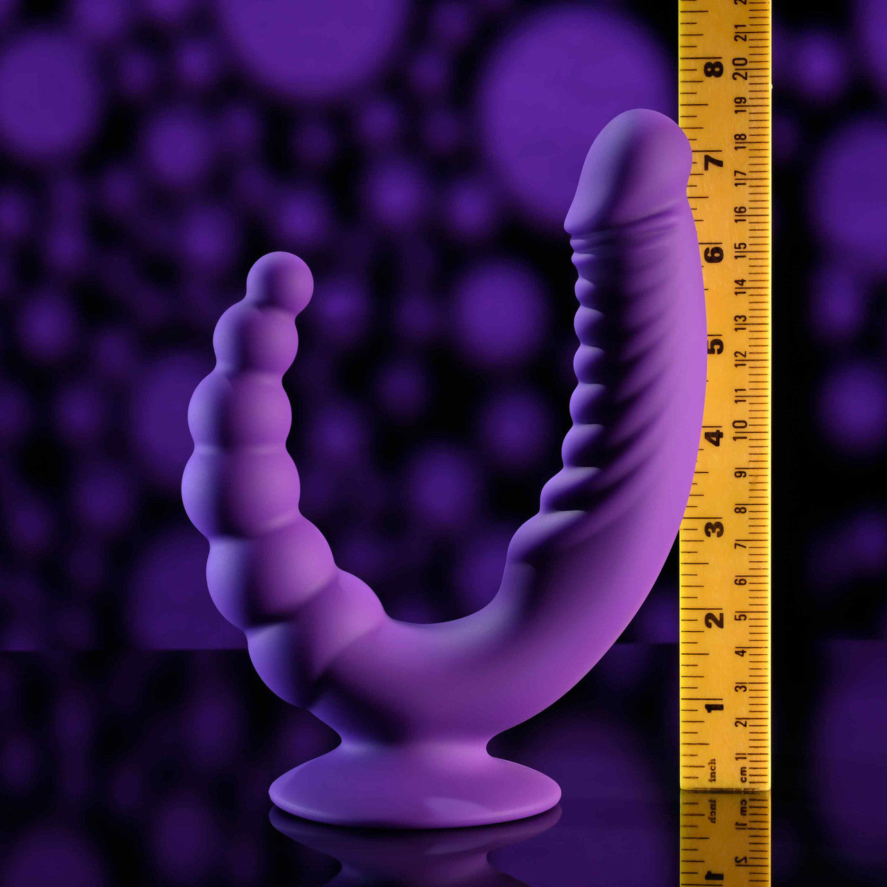A purple dual stimulating vibrator with a suction cup and a ruler for scale.