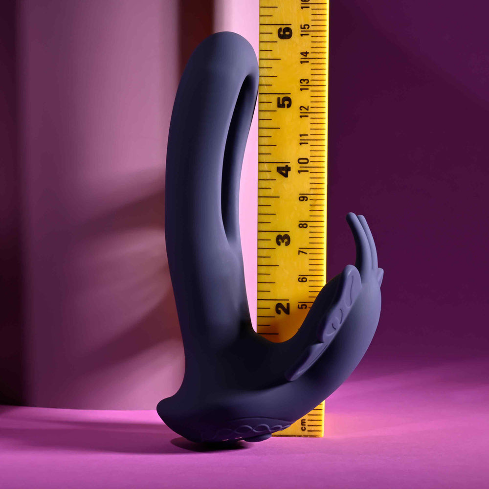 A dark purple butterfly-shaped stimulator with a ruler for scale.