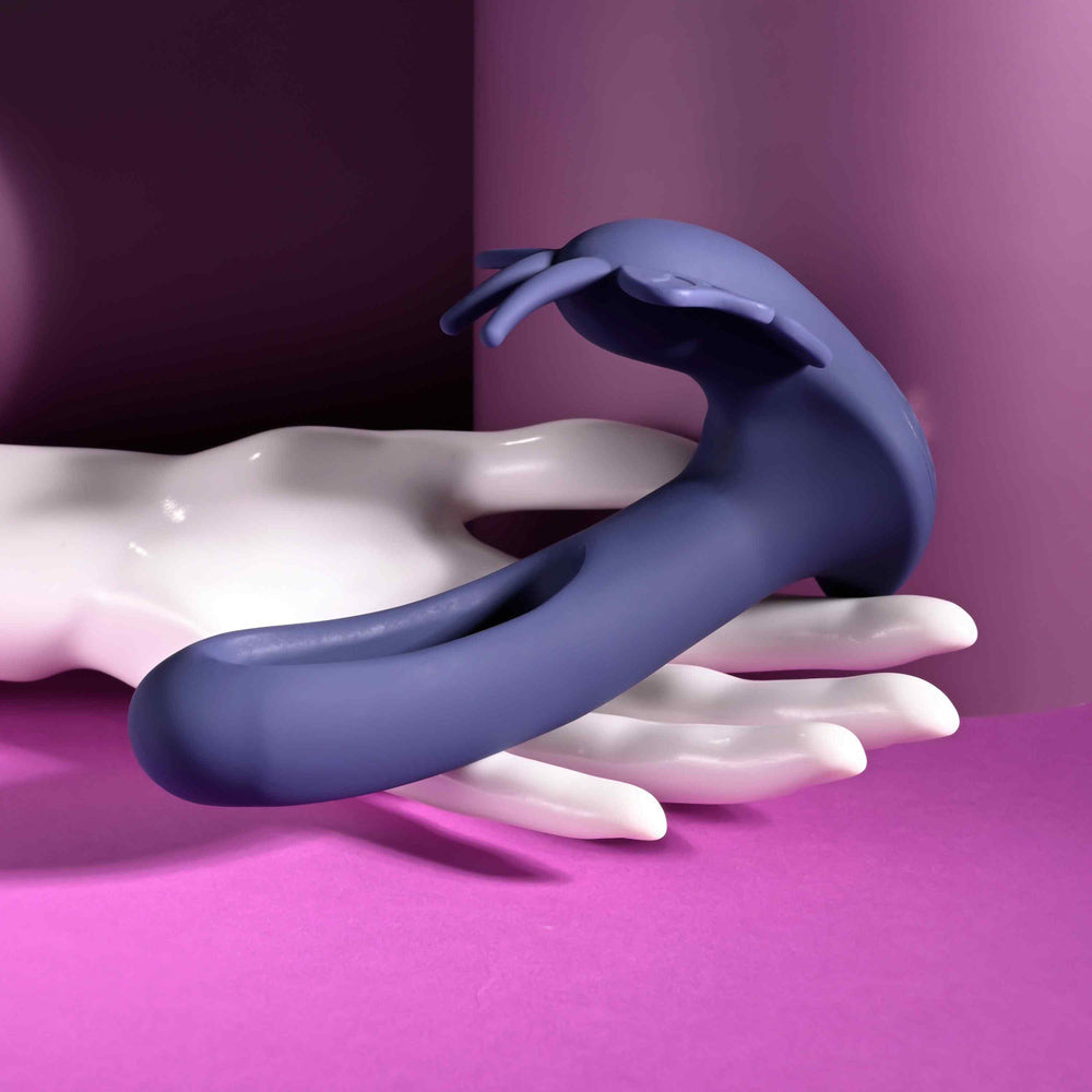 A purple butterfly-shaped stimulator rests on a white hand-like sculpture.