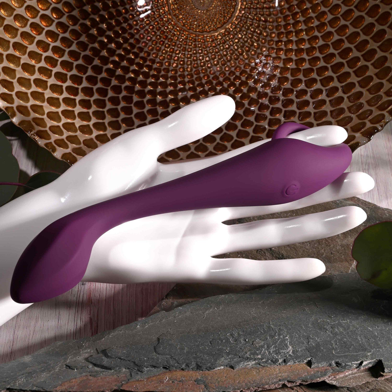A purple G-spot vibrator with a curved shaft rests on a white mannequin hand.