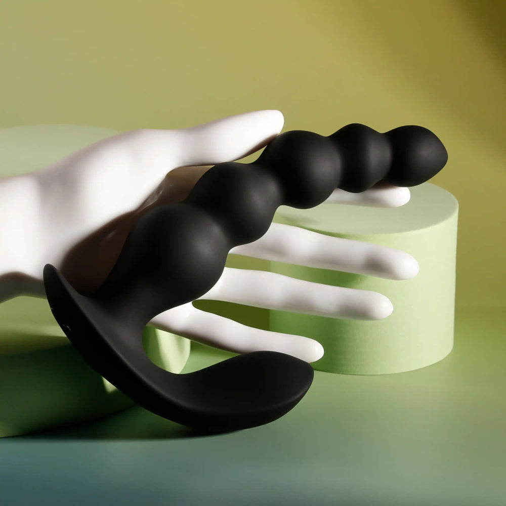 Black beaded vibrator with a curved base held by a white hand.