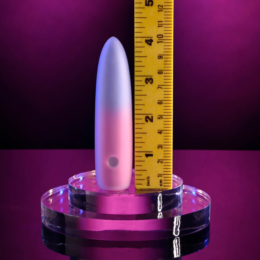 A pink and white bullet vibrator is shown next to a ruler.