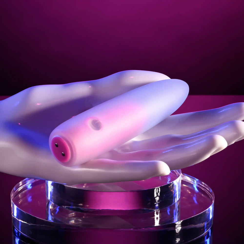 A pink and white silicone bullet vibrator rests on a white mannequin hand.