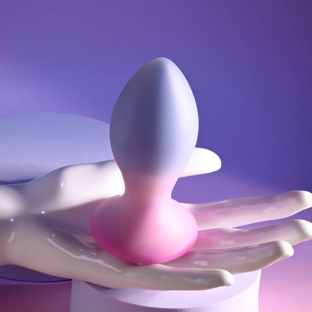A dual-toned silicone anal plug with a rounded base and tapered tip, held on a white hand sculpture.