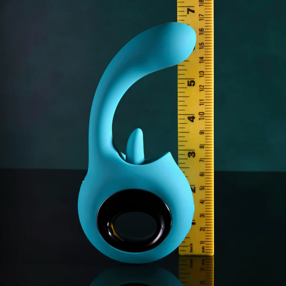 A teal silicone vibrator with a licking tongue attachment is shown next to a ruler.