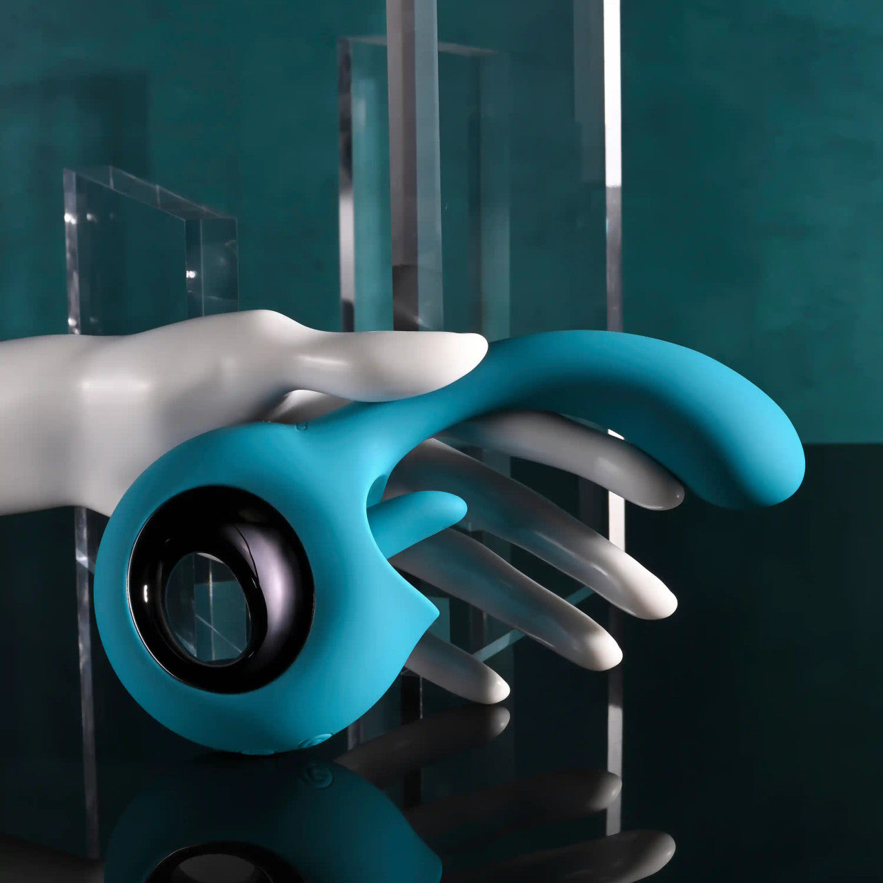 A teal licking tongue G-spot vibrator held by a white mannequin hand.