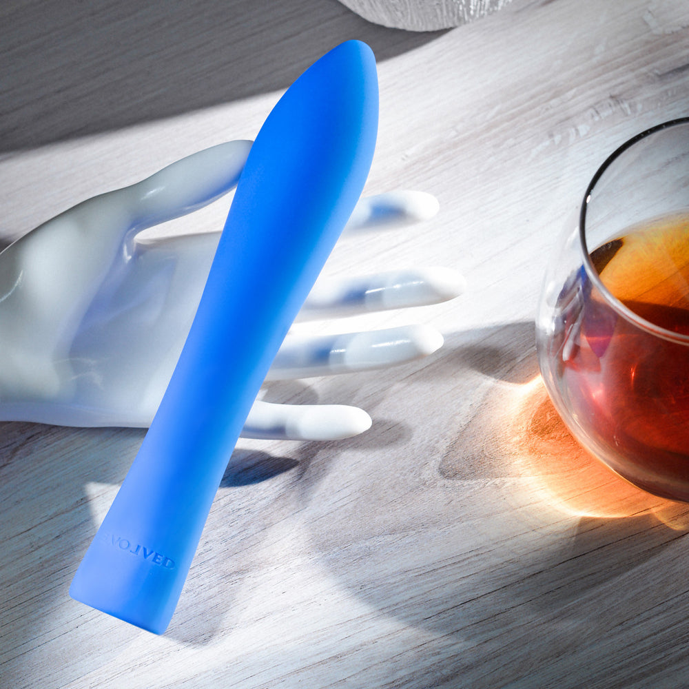 Blue silicone vibrator on a white mannequin hand next to a glass of amber liquid.