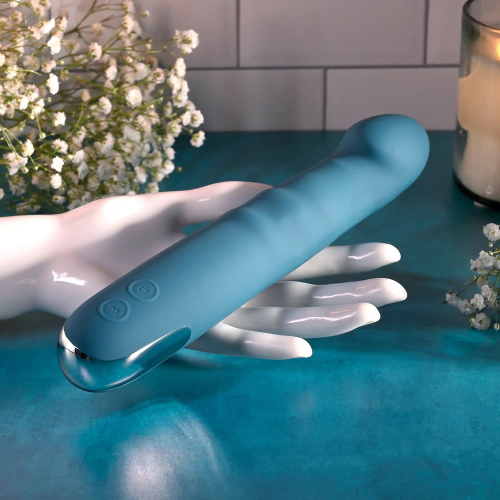A blue silicone vibrator with buttons rests on a white hand-shaped stand.