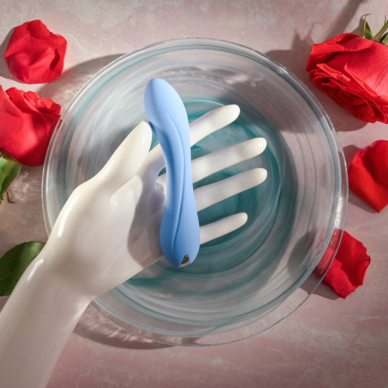 A blue silicone G-spot vibrator rests on a mannequin hand in a glass bowl.