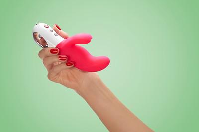 A pink and white dual motor rabbit vibrator held in a hand.