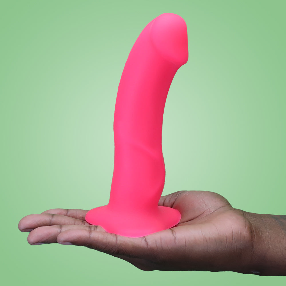 A pink realistic G-spot dildo with suction base held in a hand.