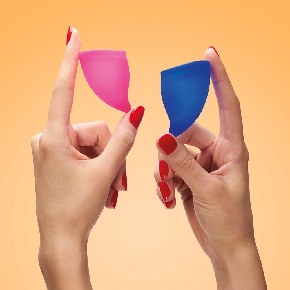 Two reusable menstrual cups, one pink and one blue, held by hands.