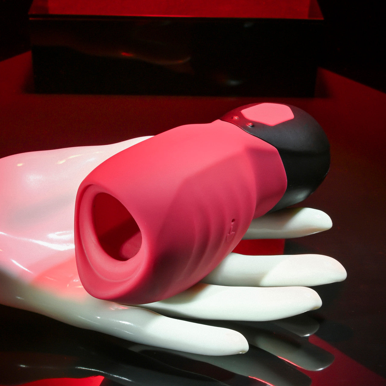 A pink and black silicone suction massager rests on a white hand mannequin.