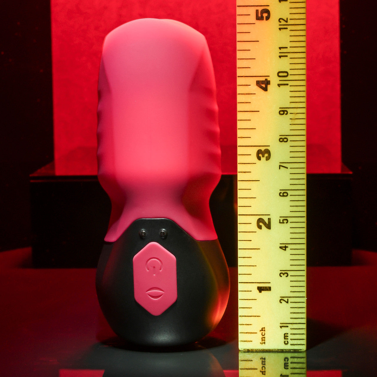A pink and black rechargeable silicone suction massager with a ruler for scale.