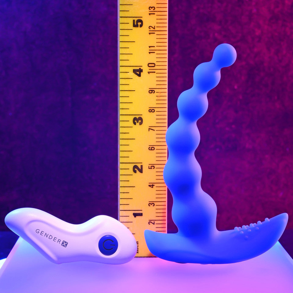 A blue beaded vibrator and a white remote are shown next to a ruler.