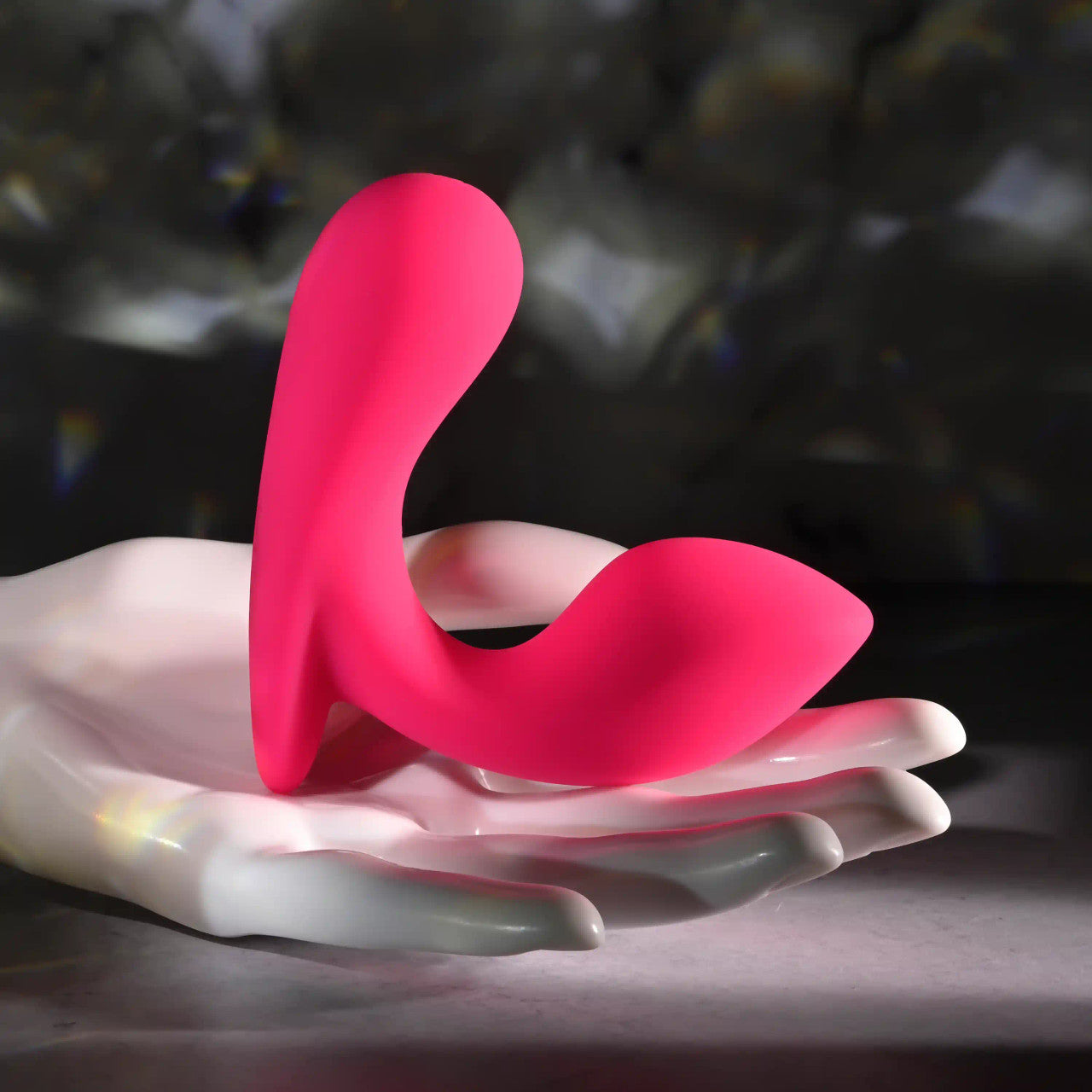 A pink curved vibrating prostate massager rests on a white hand-shaped holder.