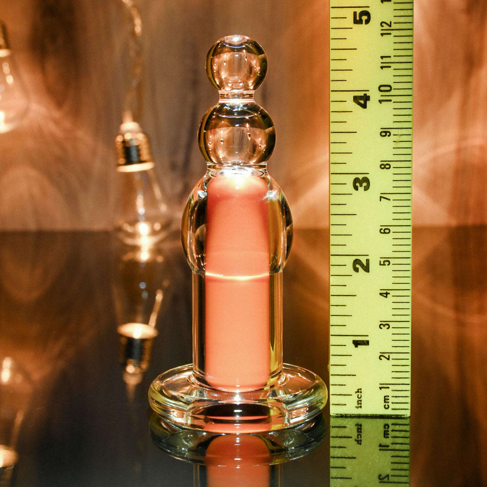 Glass beaded plug with a pink insert, next to a ruler.