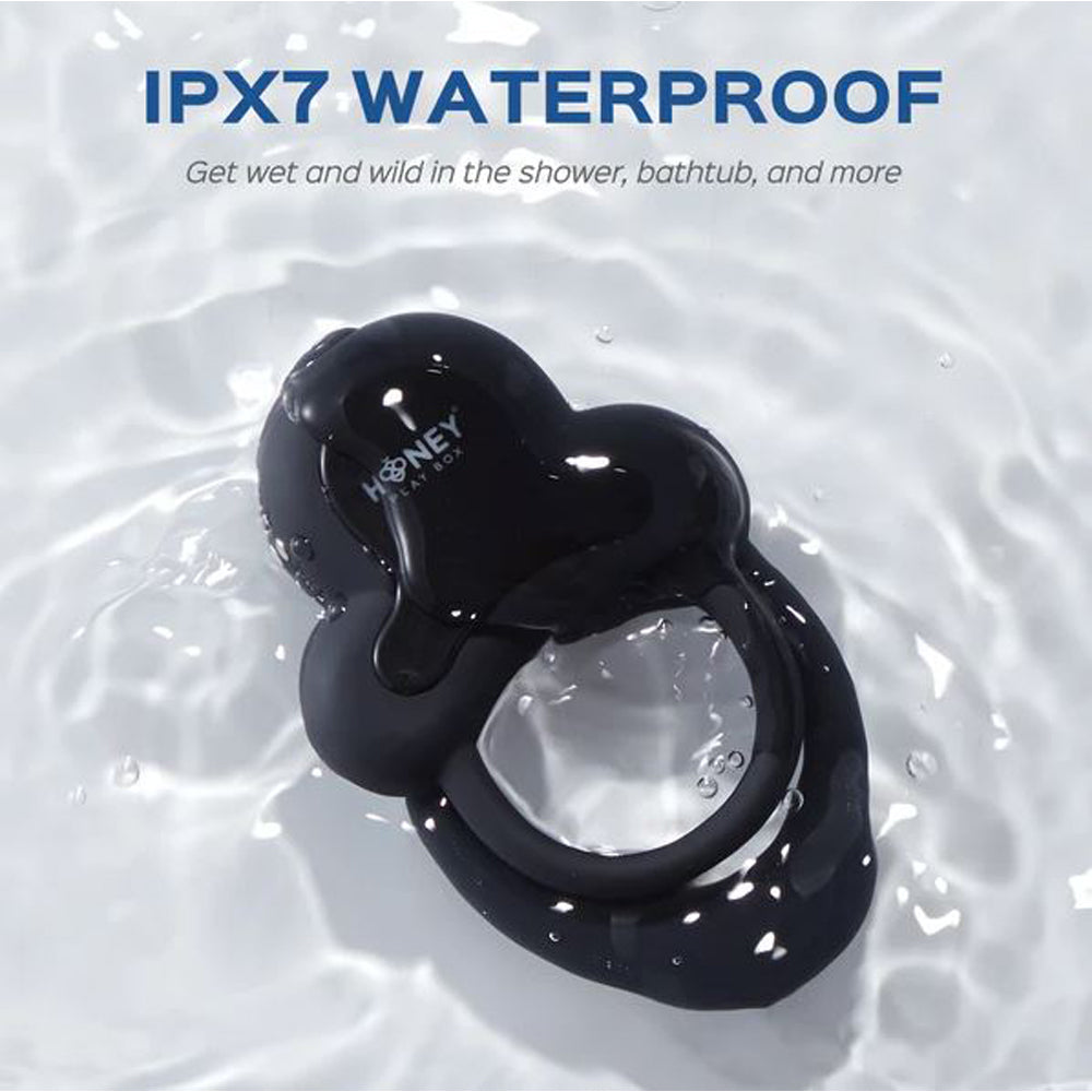 Black double cock ring with a heart-shaped top, submerged in water.