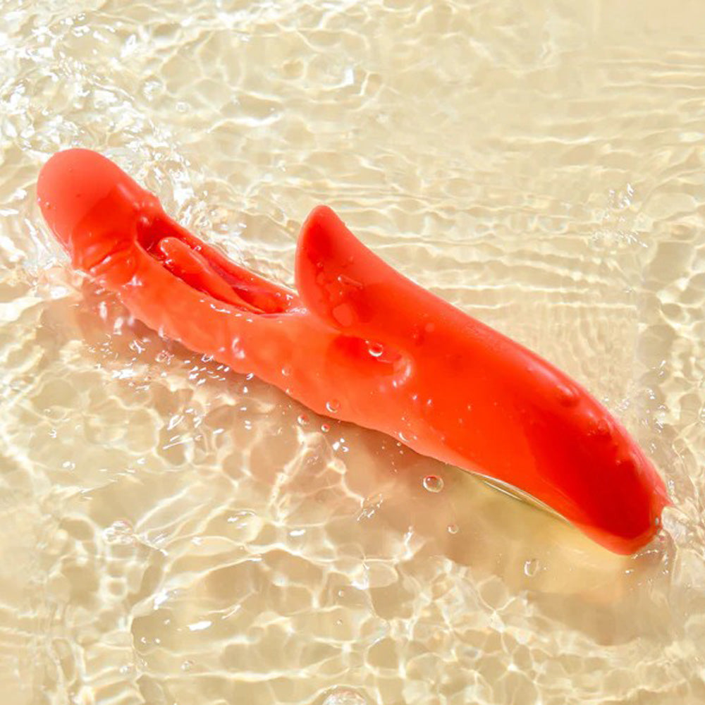 An orange rabbit vibrator with a curved shape rests in shallow water.