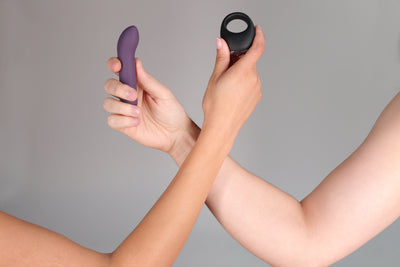 Two hands hold a purple bullet vibrator and a black cock ring vibrator.