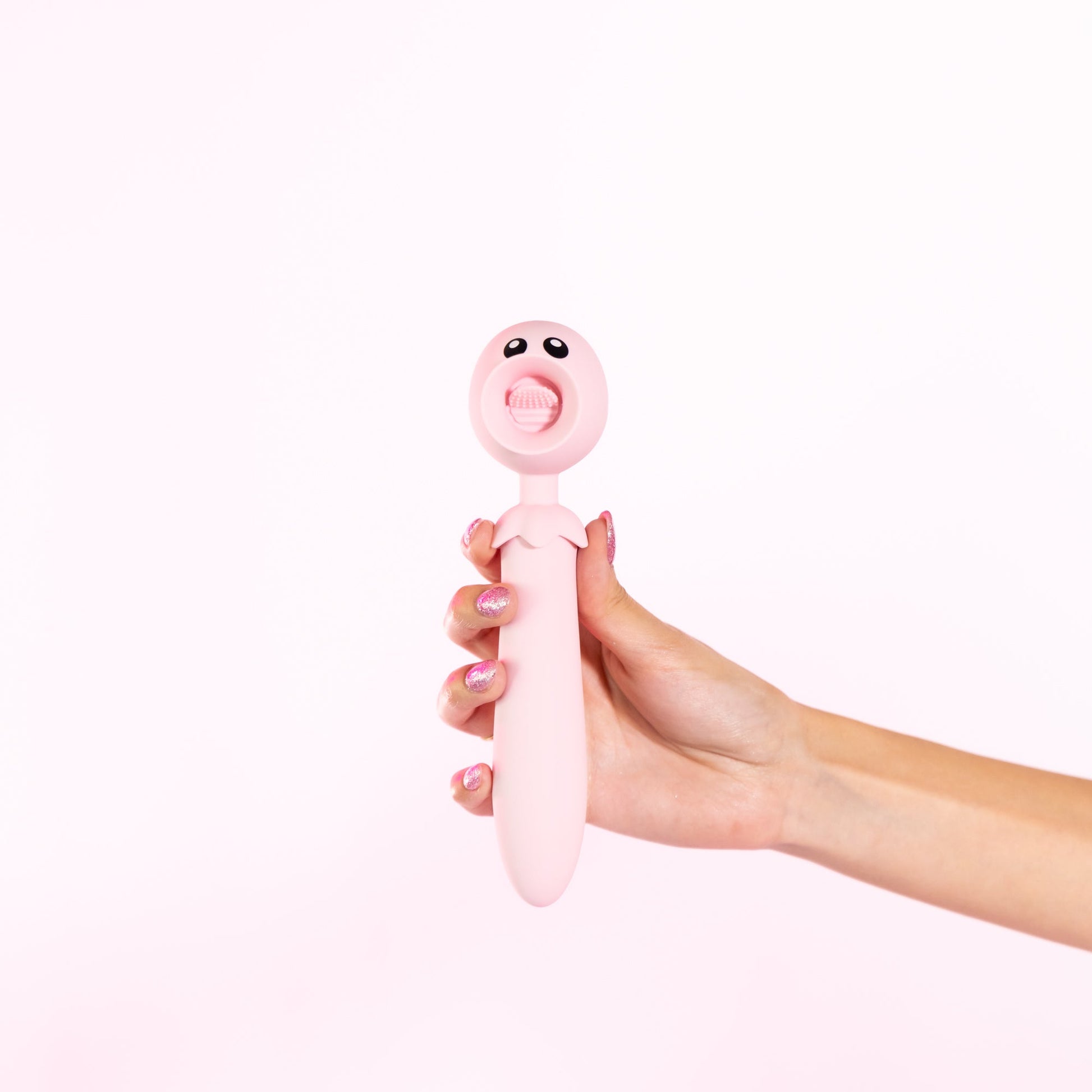 A pink, tongue-shaped vibrator with eyes, held by a hand with glittery nails.