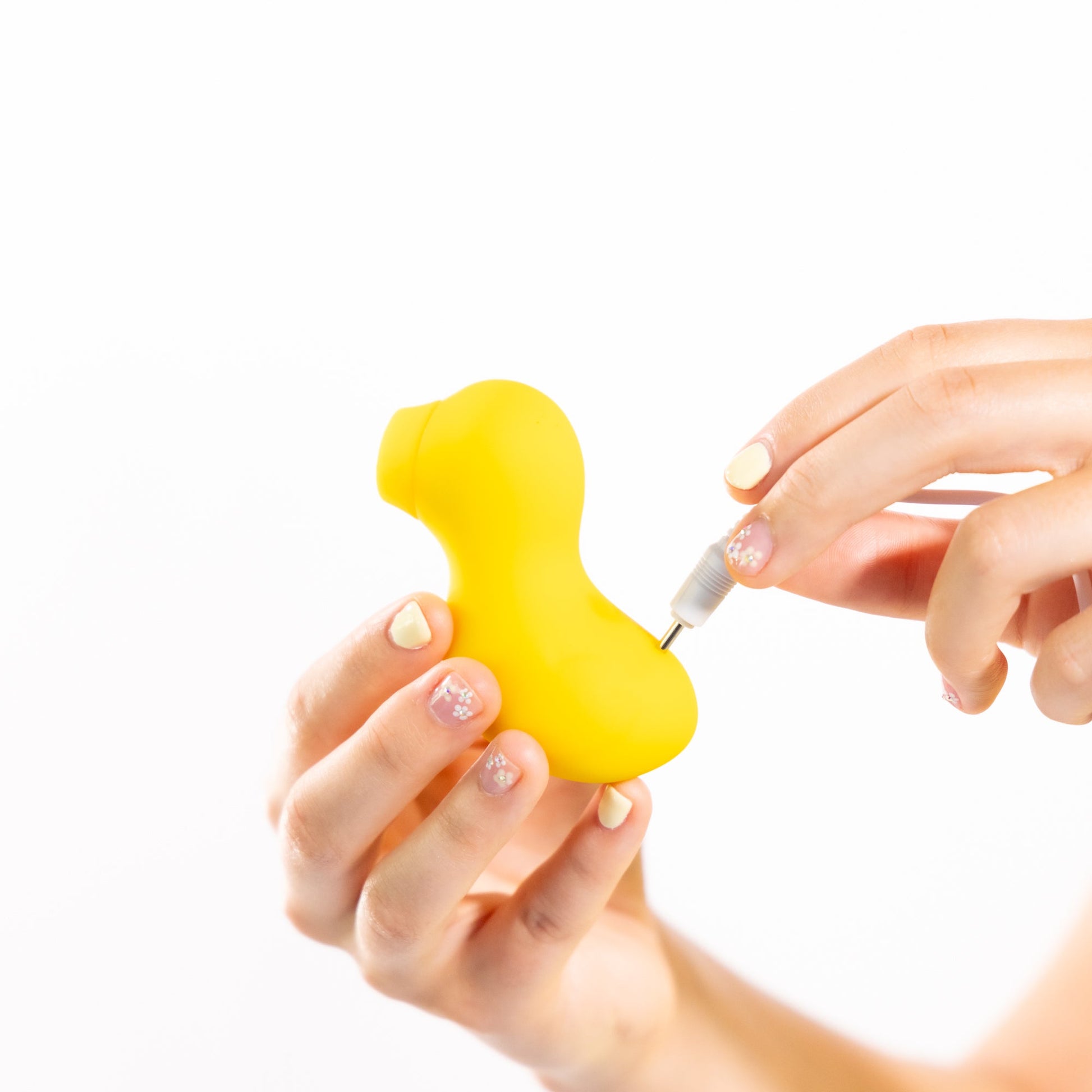 A yellow duck-shaped silicone stimulator with a charging cable being inserted.