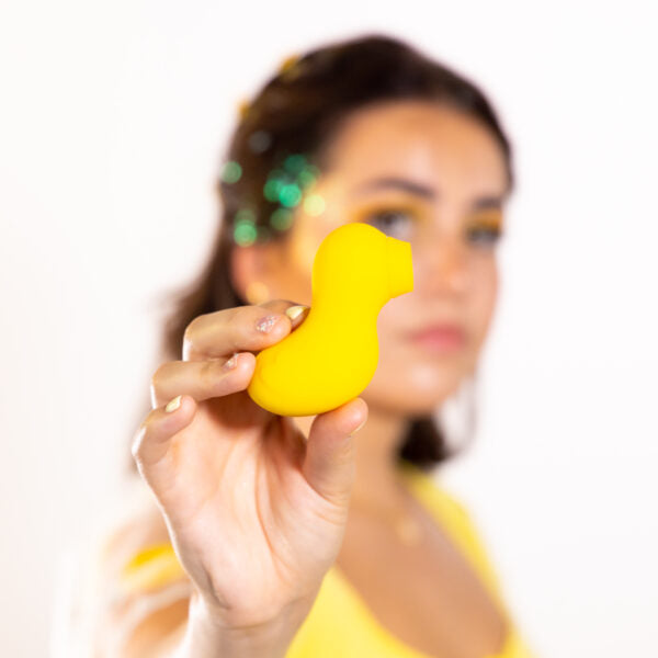 Yellow duck-shaped silicone suction stimulator held by a person.