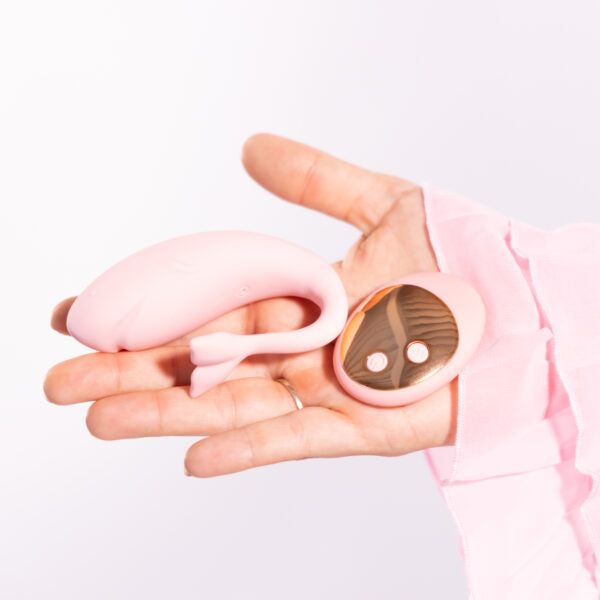 A pink whale-shaped wearable vibrator and remote control held in a hand.