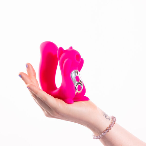A pink squirrel-shaped vibrator with silver buttons held in a hand.