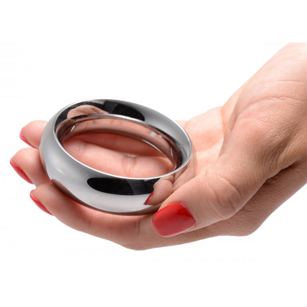 A polished stainless steel cock ring rests in a hand with red nail polish.