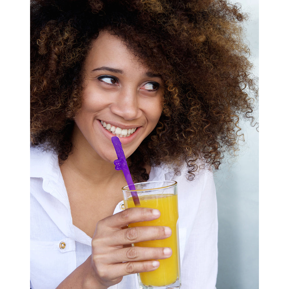 A woman smiles while drinking from a glass of orange juice with a purple novelty straw.