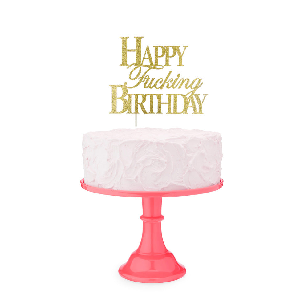 Gold glitter cake topper with "Happy Fucking Birthday" text on a pink cake stand.