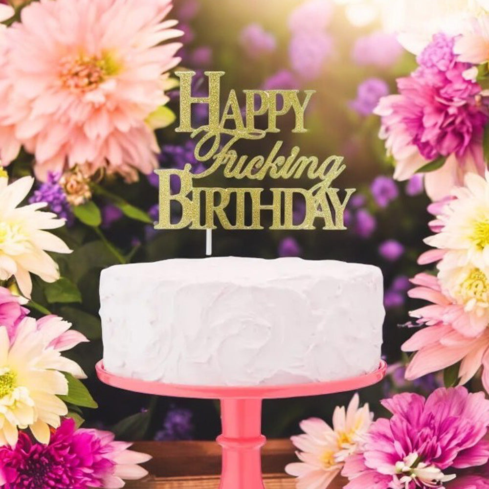 Gold glitter "Happy Fucking Birthday" cake topper surrounded by flowers.