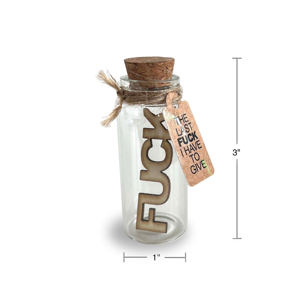 Glass jar with cork lid, wooden letters spelling "FUCK" and a tag that says "THE LAST FUCK I HAVE TO GIVE".