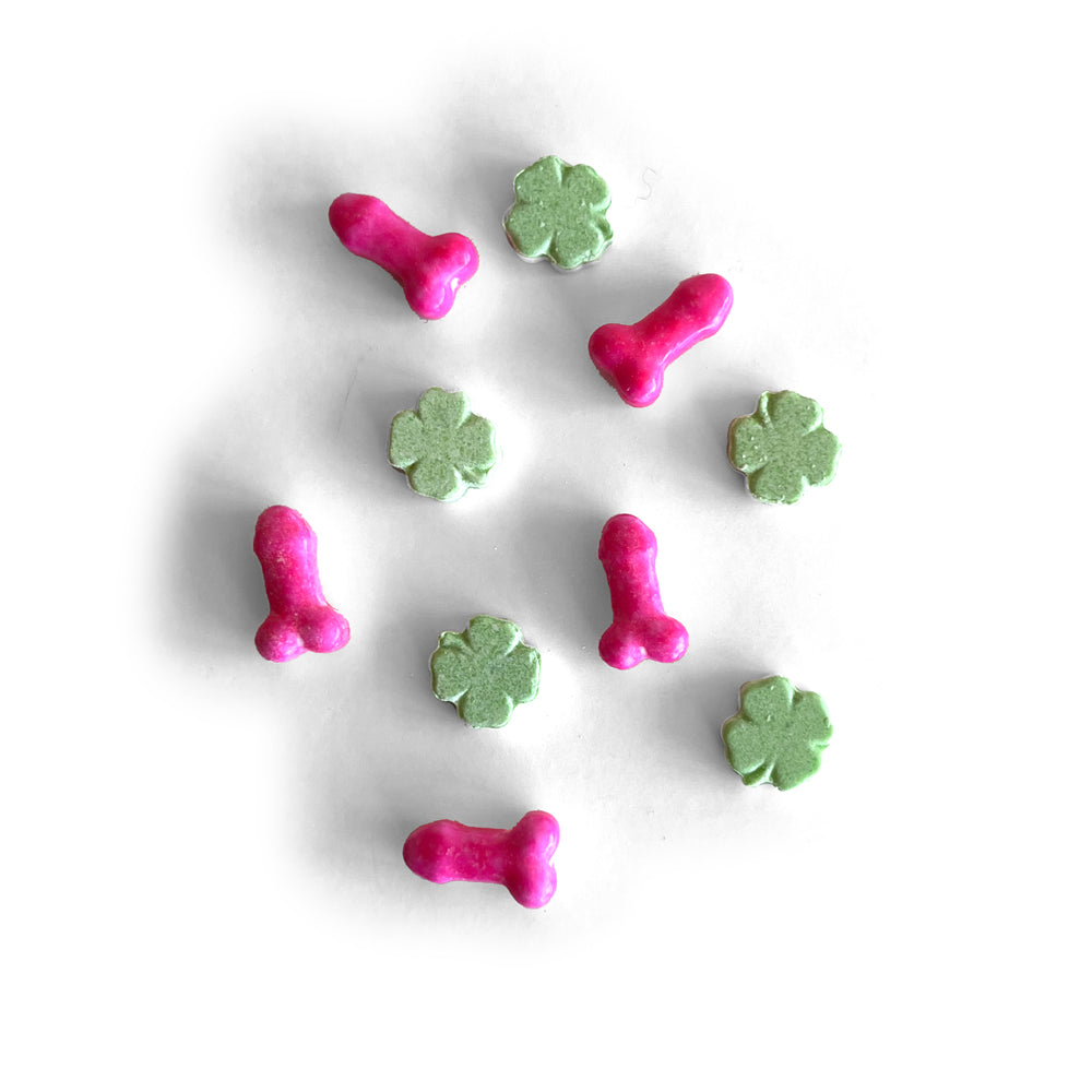 Pink penis-shaped candies and green shamrock candies scattered on a white surface.