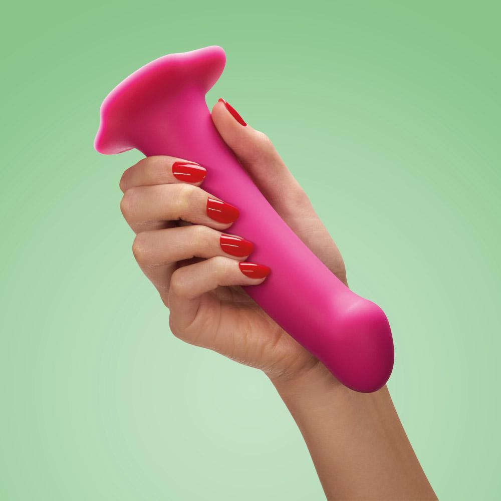 Pink silicone dildo with a suction base held by a hand.
