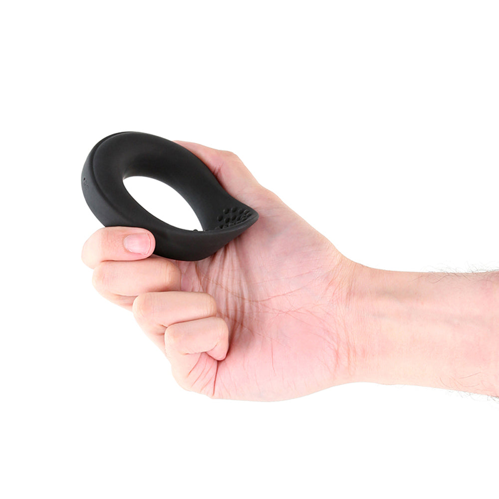 A black vibrating cock ring with textured dots is held in a hand.