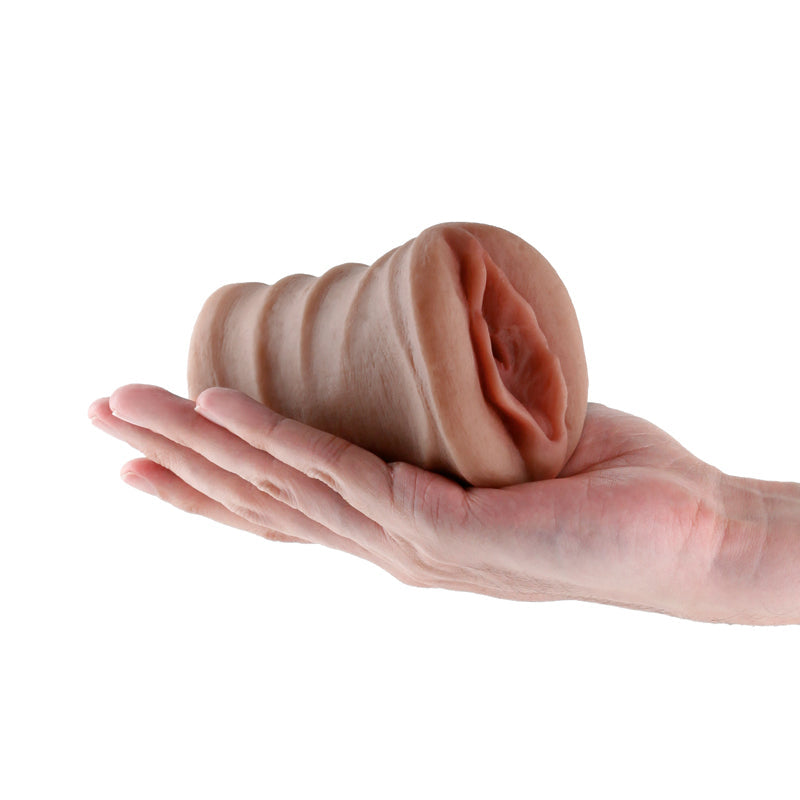 A hand holds a realistic brown TPE male stroker with textured shaft and lifelike vaginal opening.