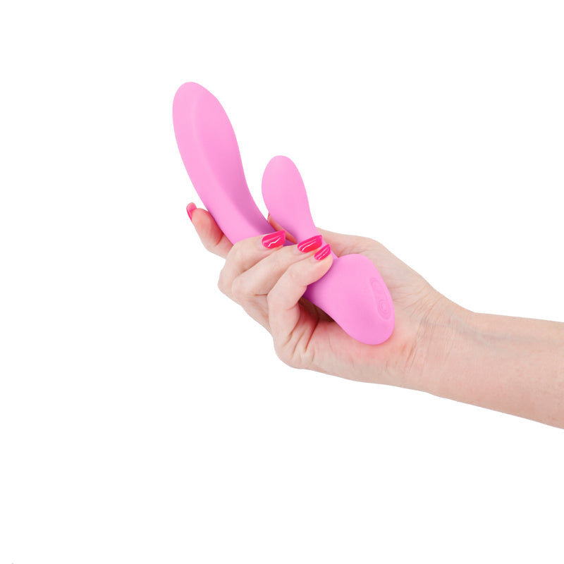 A hand holds a light pink silicone vibrator with two curved ends.