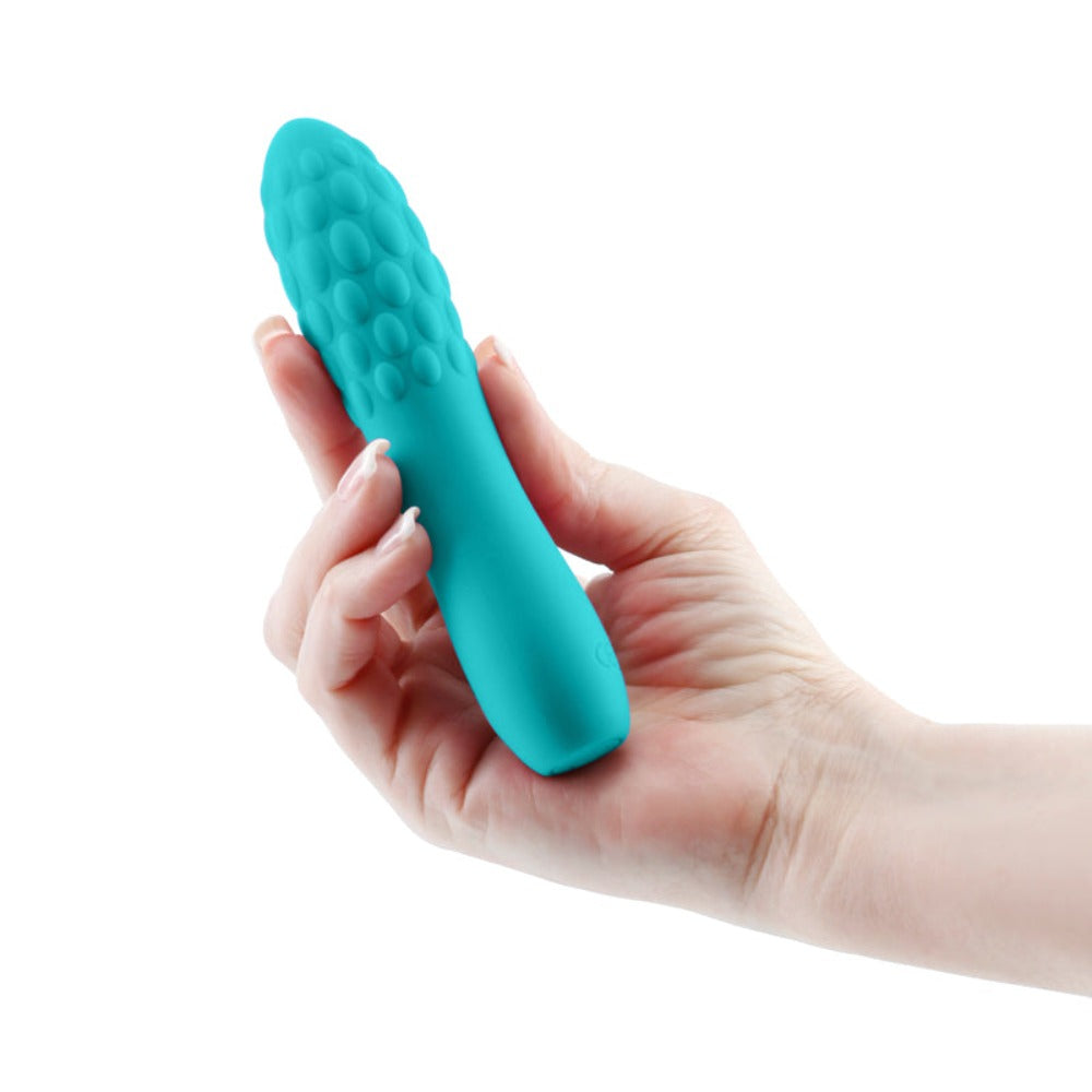Teal silicone massager with textured head held in a hand.