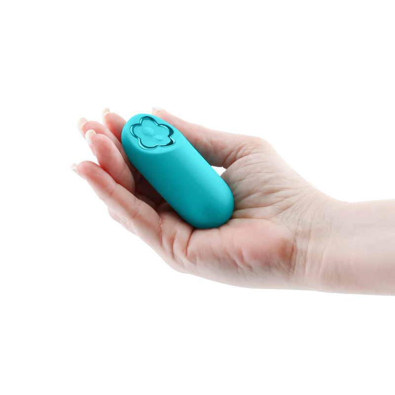 A teal mini silicone vibrator with a flower-shaped button rests in a person's palm.